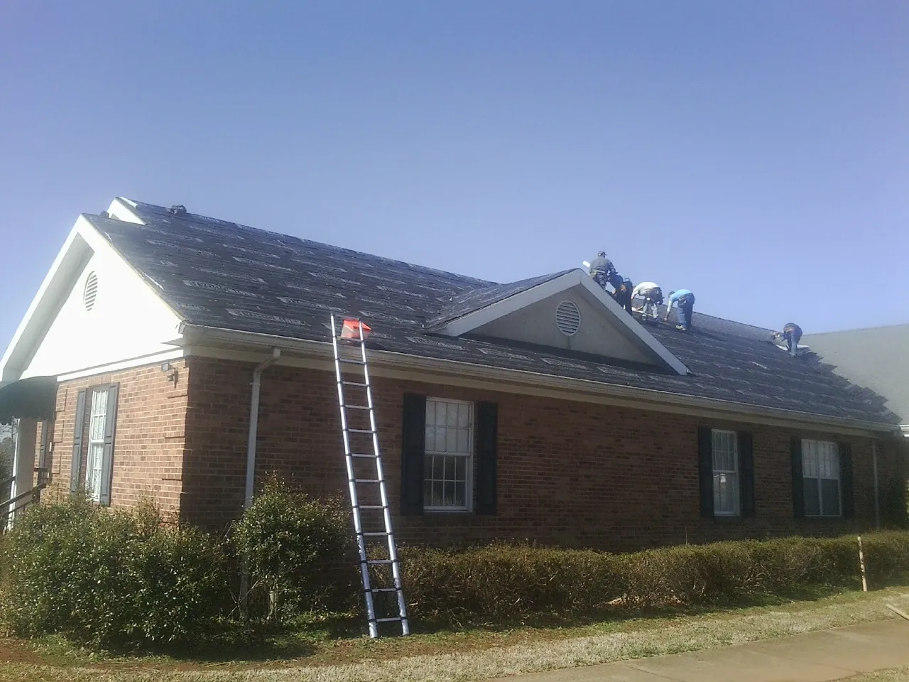 Crew tearing shingles off a brick ranch roof with a ladder set — Emergency Roof Repair work by our crew in Fort Mitchell