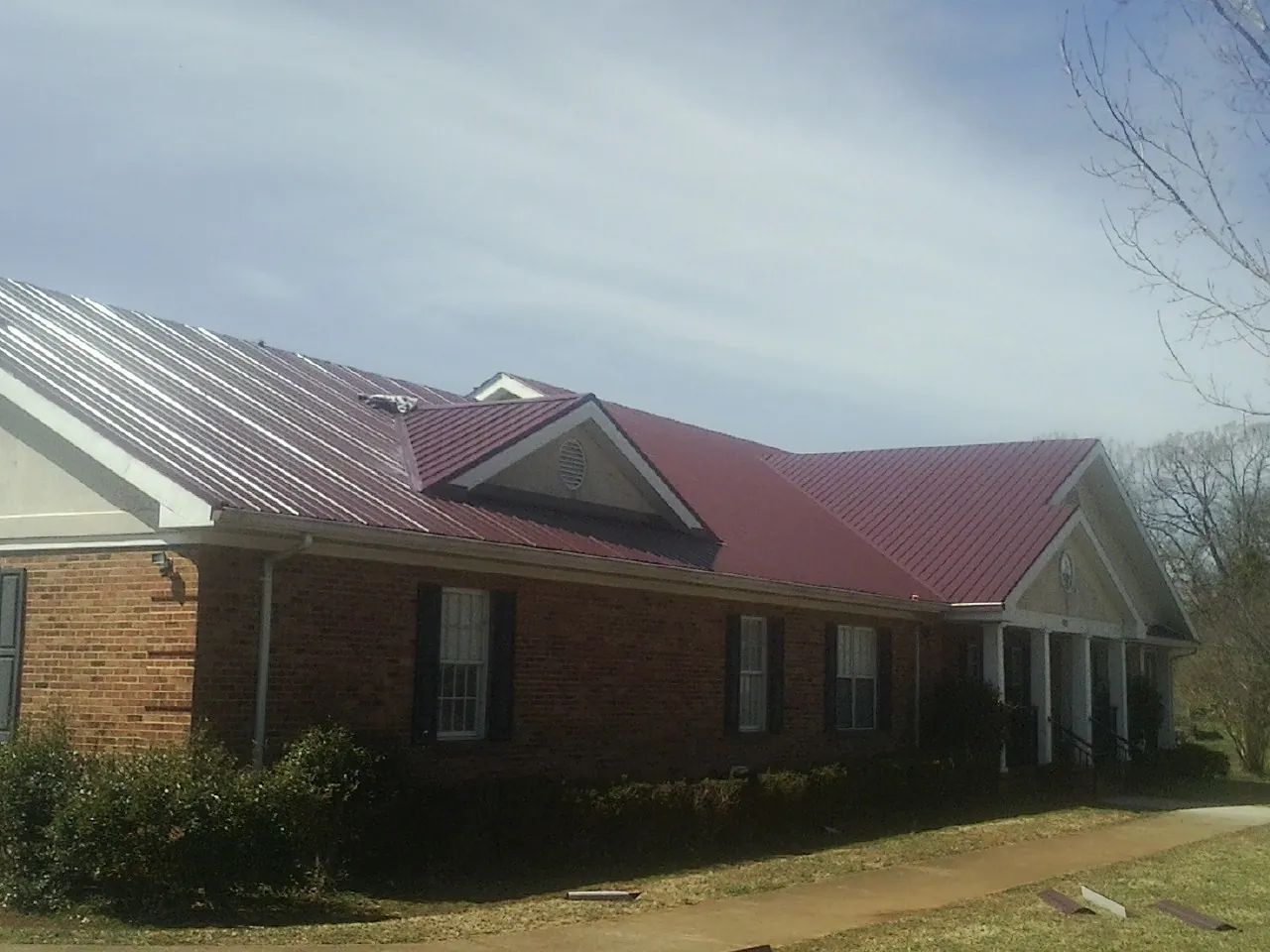 Red metal roof with gabled entries on a long brick building, from a Hail Damage Roof Repair job in Fort Mitchell