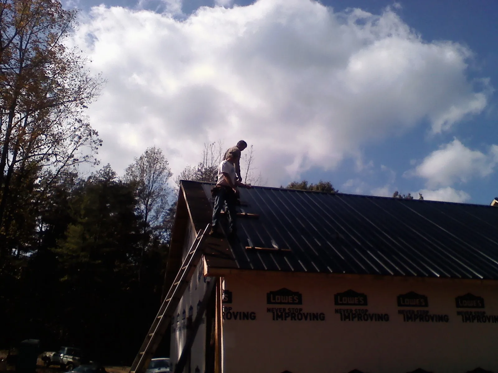 Roofer fastening dark metal panels high against a cloudy sky, from a Roof Inspection job in Fort Mitchell