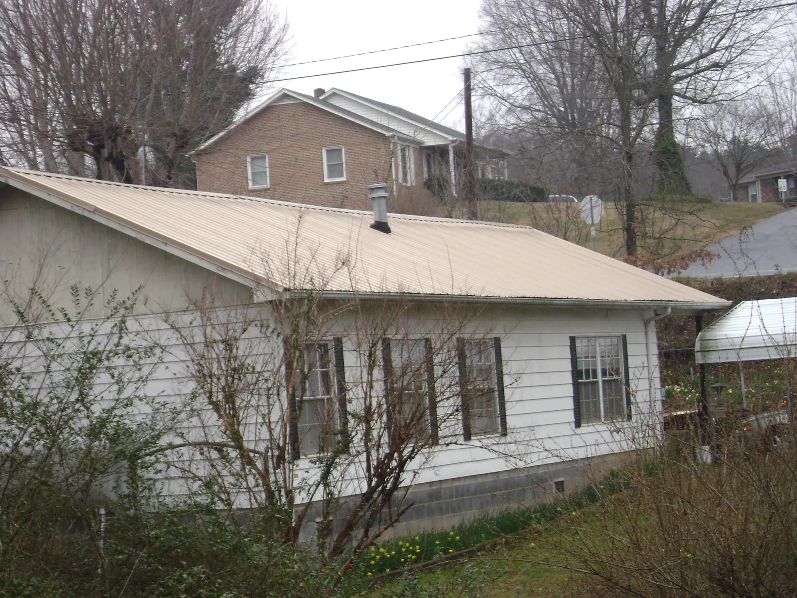 Tan metal roof on a white sided house set into a hillside — Commercial Roofing by Roofing Brothers in Fort Mitchell